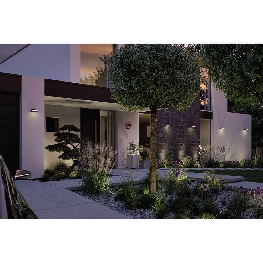 Solar LED Außenwandleuchte Ronas mit Sensor Dunkelgrau an einem modernen Haus mit schönem Garten und Pflanzen.
