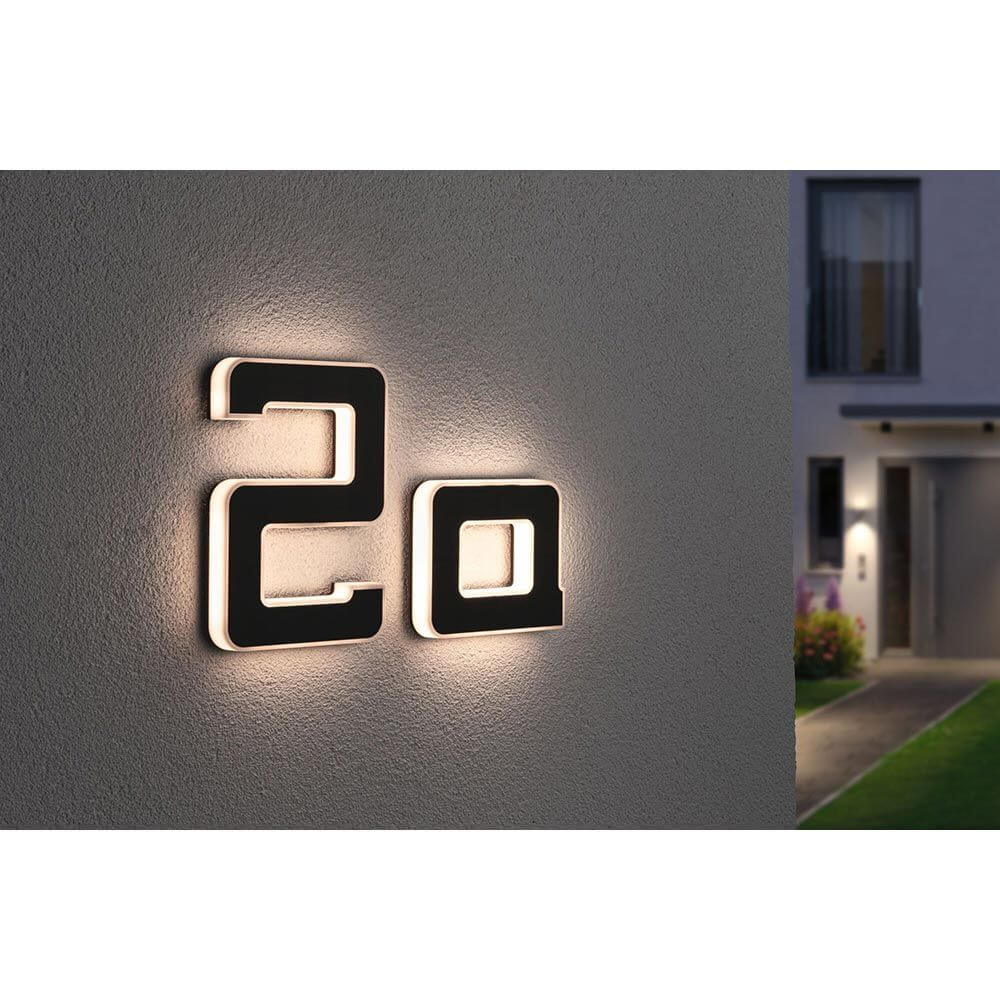 LED Solar Hausnummernleuchte Buchstabe A Schwarz an einer Hauswand montiert, beleuchtet bei Nacht.