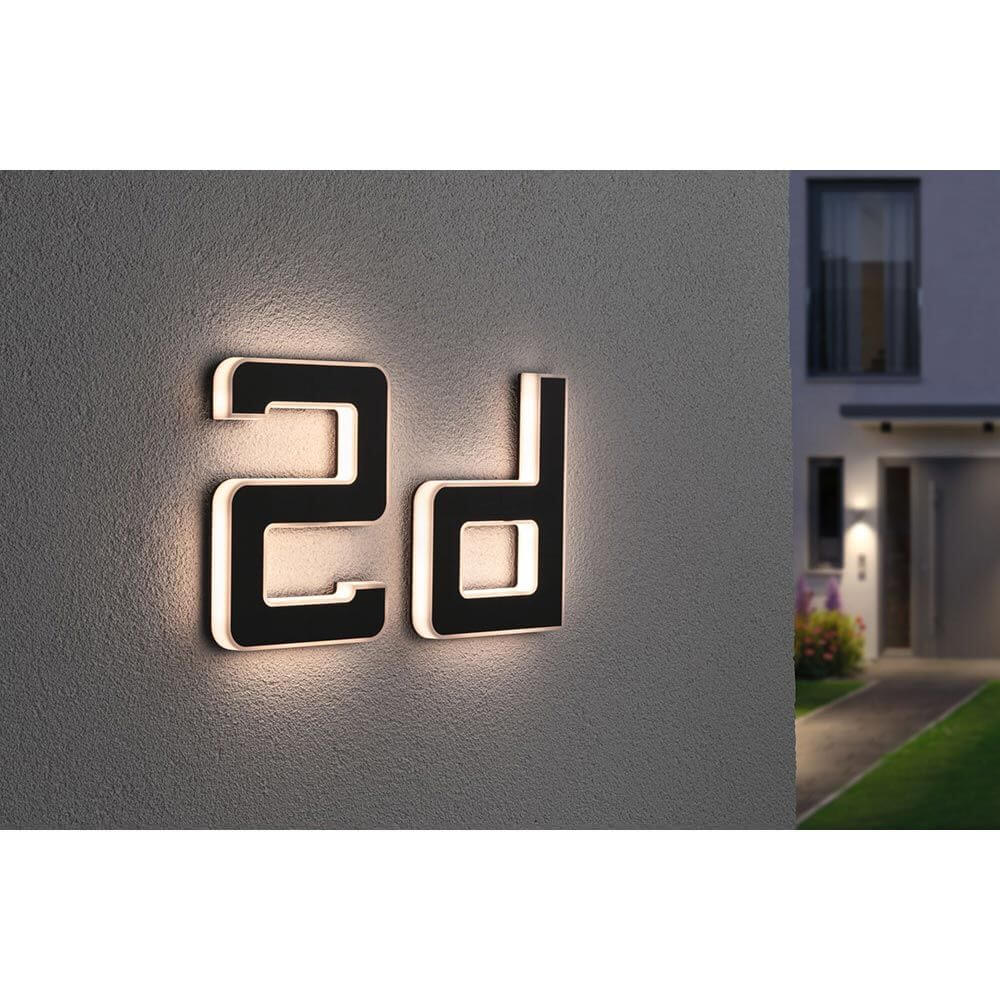Solar LED Hausnummernleuchte Buchstabe D in Schwarz, warmweiße Beleuchtung bei Nacht an der Hauswand.