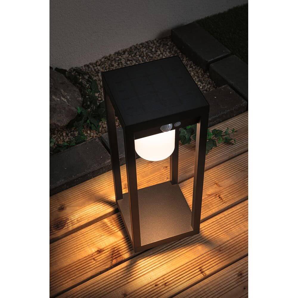 Solar LED Sensor Laterne Marisol Schwarz bei Nacht, warmweißes Licht auf Holzdeck, ideal für Wege und Eingangsbereiche.