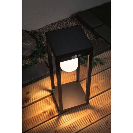Solar LED Sensor lantern Marisol Black on a wooden terrace, warm white light powered by solar technology.
