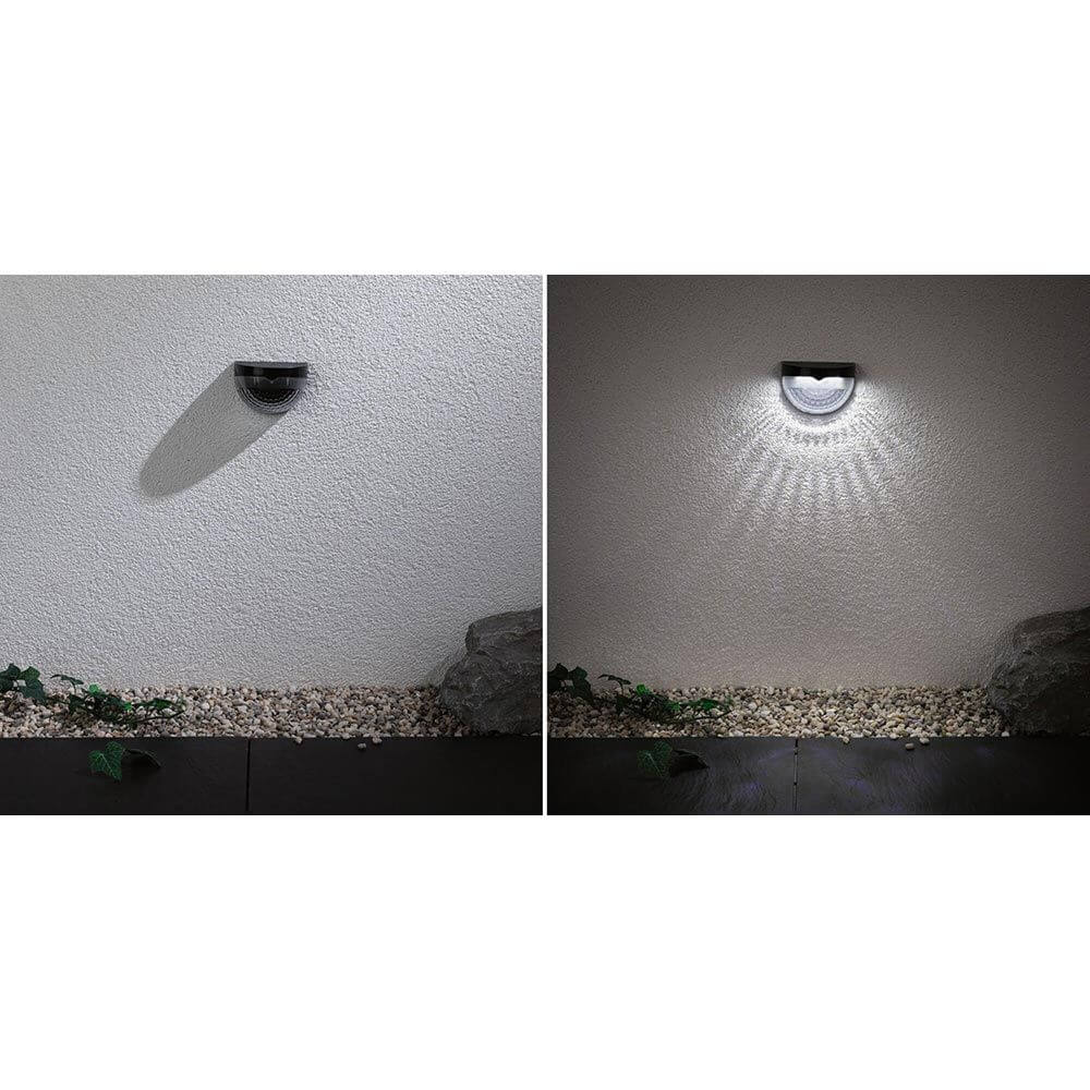 Solar LED Wegeleuchte Mimmo Schwarz an einer Wand, leuchtend im Dunkeln mit Schattenwurf.
