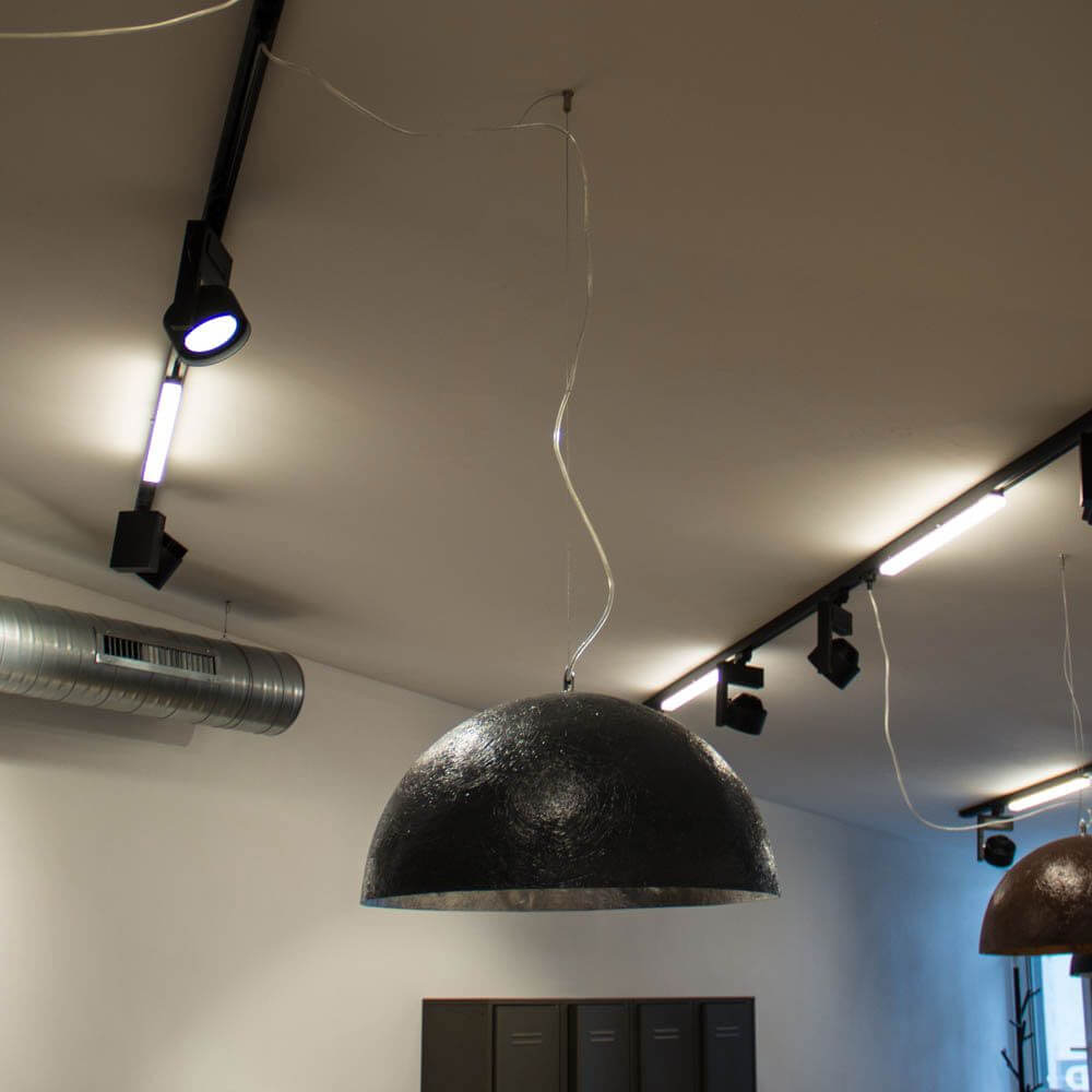 Hängeleuchte mit schwarzem Schirm und Stahlseilhalter im modernen Innenraum.