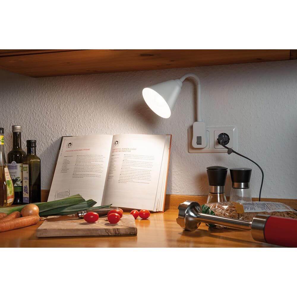 Steckerleuchte Junus Flexarm Weiß leuchtet über offenem Rezeptbuch auf einem Küchenarbeitsplatz.