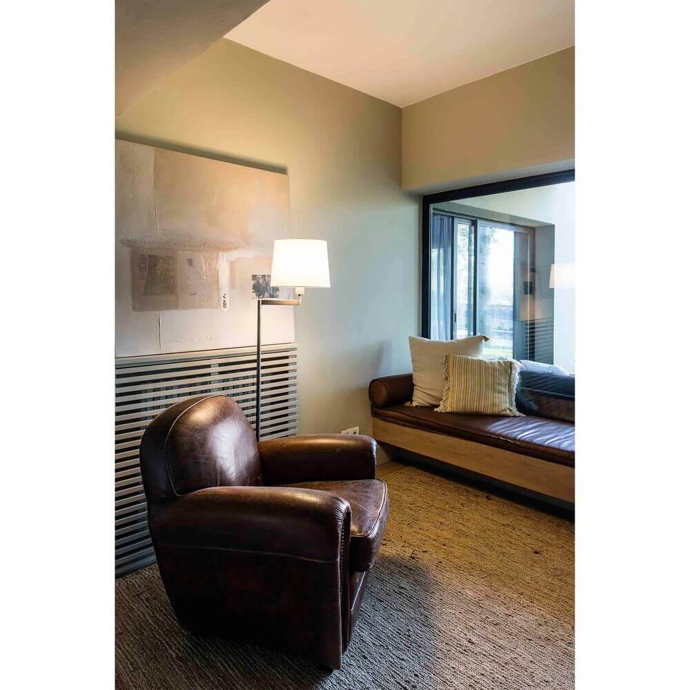 Stehlampe ARTIS Bronze, Weiß neben einem bequemen Sessel in einem hellen Wohnraum.