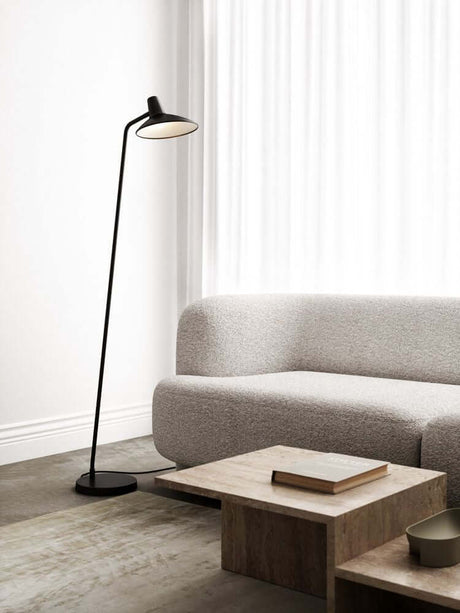 Lampe sur pied Darci stylée dans un design d’intérieur moderne, à côté d’un canapé gris et d’une table.