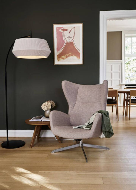 Stehlampe Dicte neben einem modernen Sessel in einem stilvollen Wohnzimmer, schafft Gemütlichkeit und Atmosphäre.