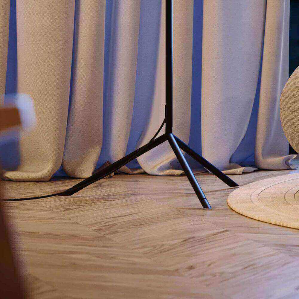 Moderne Stehlampe mit einem minimalistischen schwarzen Standfuß, umgeben von blauen Vorhängen und einem runden Teppich.