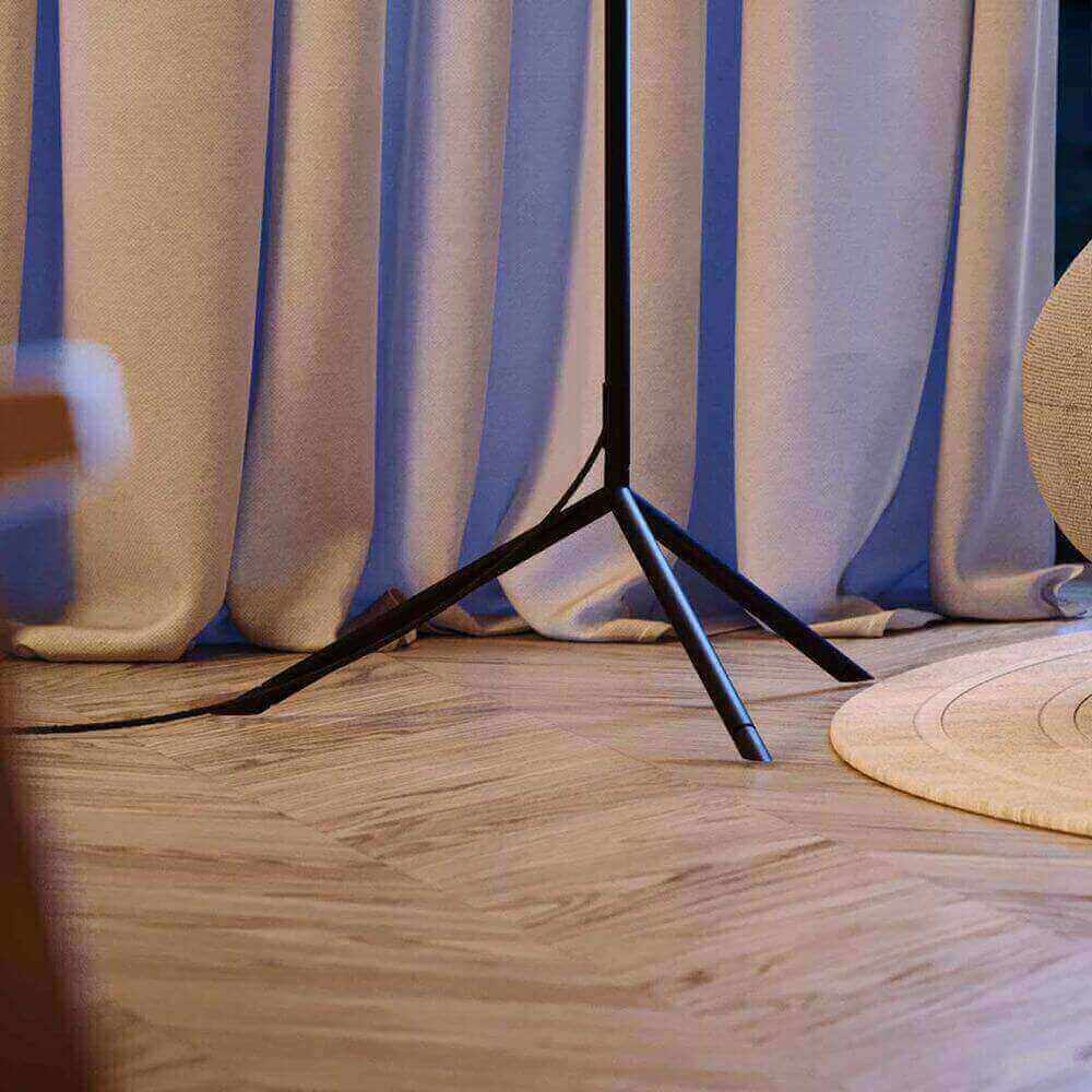 Moderne Stehlampe mit einem minimalistischen schwarzen Standfuß, umgeben von blauen Vorhängen und einem runden Teppich.