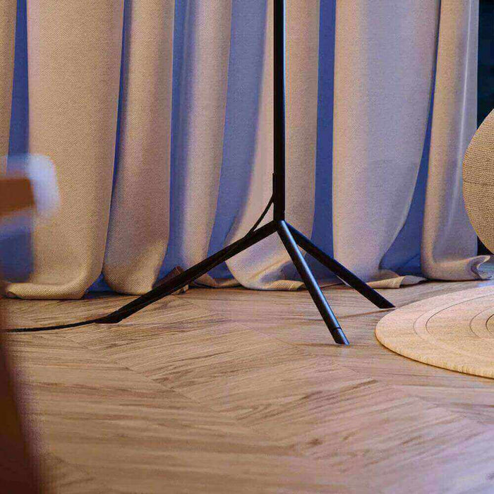 Moderne Stehlampe mit einem minimalistischen schwarzen Standfuß, umgeben von blauen Vorhängen und einem runden Teppich.