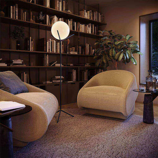 Gemütlicher Wohnraum mit beigen Sesseln, moderner Stehlampe und Bücherregal im Hintergrund.