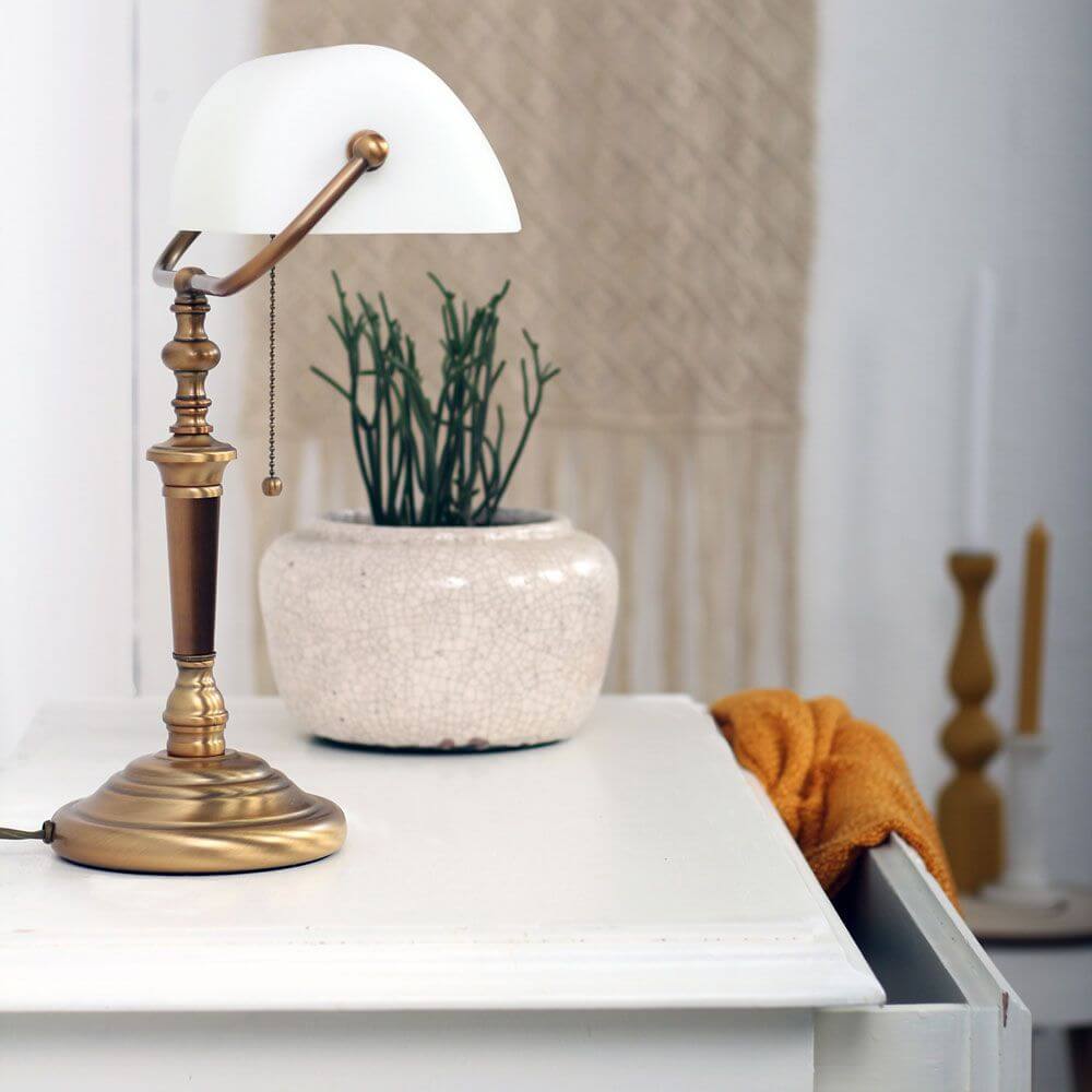 Vintage Tischleuchte Ancilla mit bronze-gebürstetem Fuß und Glas-Schirm auf einem Tisch.