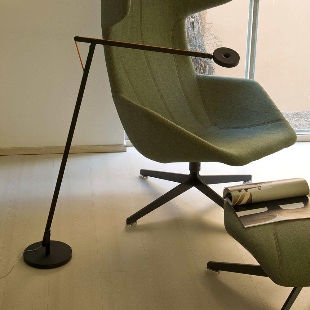 Lámpara de pie LED Rotaliana String con Push Dimm to Warm en plata junto a un sillón moderno en una habitación elegante.