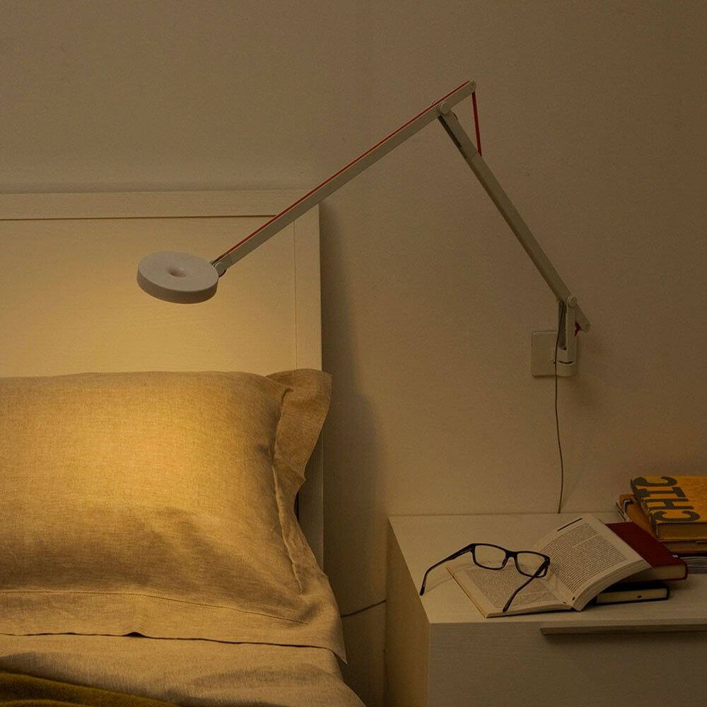 Rotaliana String LED-Wandleuchte mit Dimmer Schwarz über einem Bett mit Bücher und Brille.