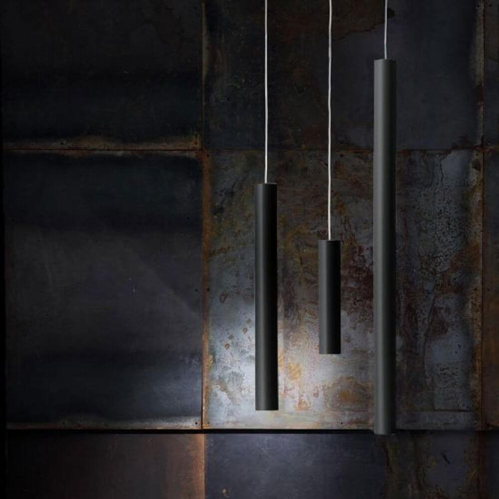 Lodes A-Tube Hängeleuchte GU10 in schwarzem Design, hängend in verschiedenen Längen vor einer rustikalen Wand.