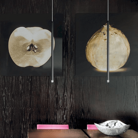 Suspension Lodes A-Tube Nano LED au-dessus d’une table à manger moderne avec des œuvres d’art en arrière-plan.