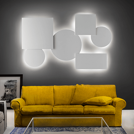 Lodes Puzzle Mega Round Ø 80 cm applique murale et plafonnier blanc, installation lumineuse géométrique au-dessus d’un canapé jaune.