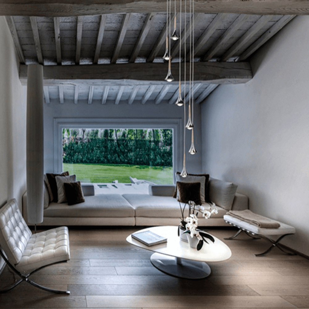 Modernes Wohnzimmer mit Lodes Rain LED Hängelampe, eleganten Möbeln und Blick ins Grüne.