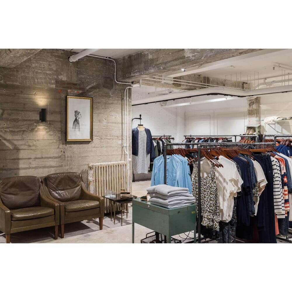 Moderne Boutique mit Kleidung auf Kleiderständern und gemütlichen Lederstühlen im Vordergrund.