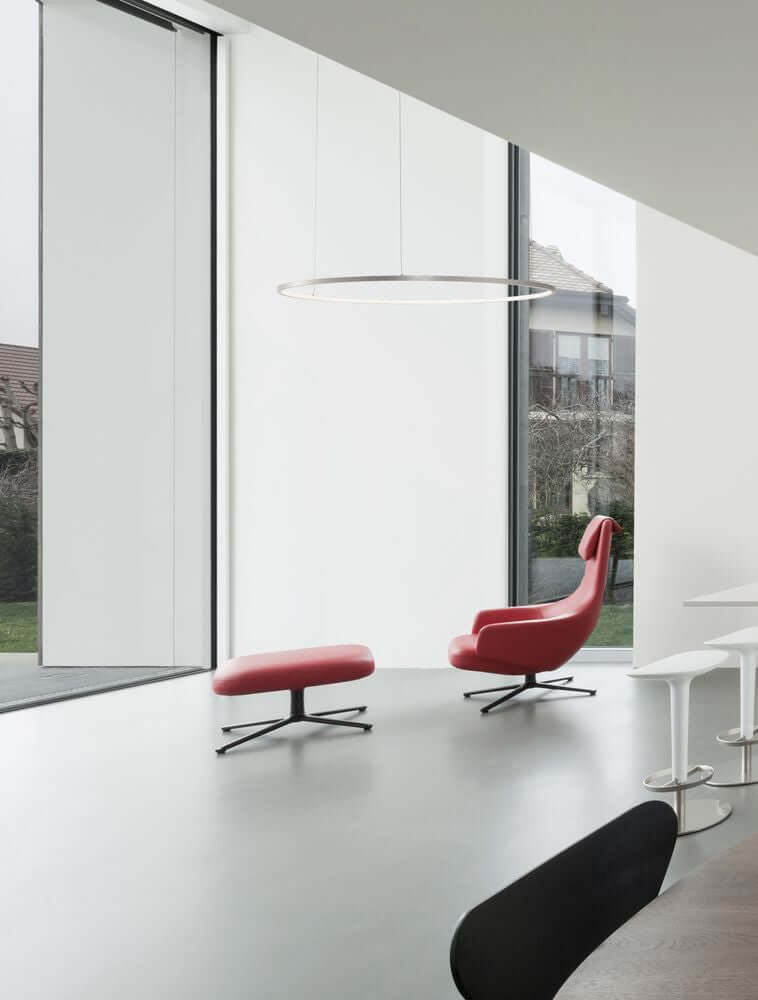Moderne Innenansicht mit Tarquin LED Pendelleuchte, rotem Sessel und großen Fenstern.