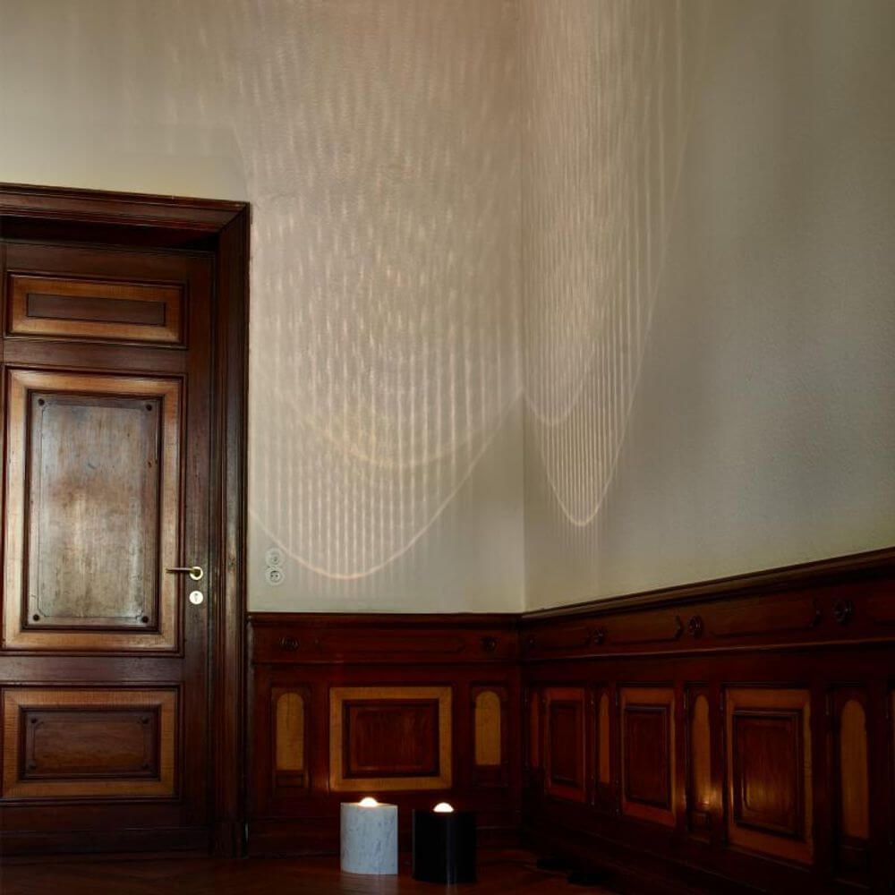 Tecnolumen Egyptian Eye Bodenlampe in einem stilvollen Raum mit einzigartigem Lichtmuster an der Wand.