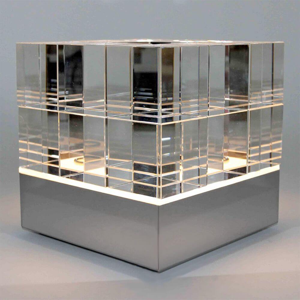 Tecnolumen Tischleuchte Cubelight Edelstahl Glas klar schwarz rosa auf einem minimalistischen Hintergrund.