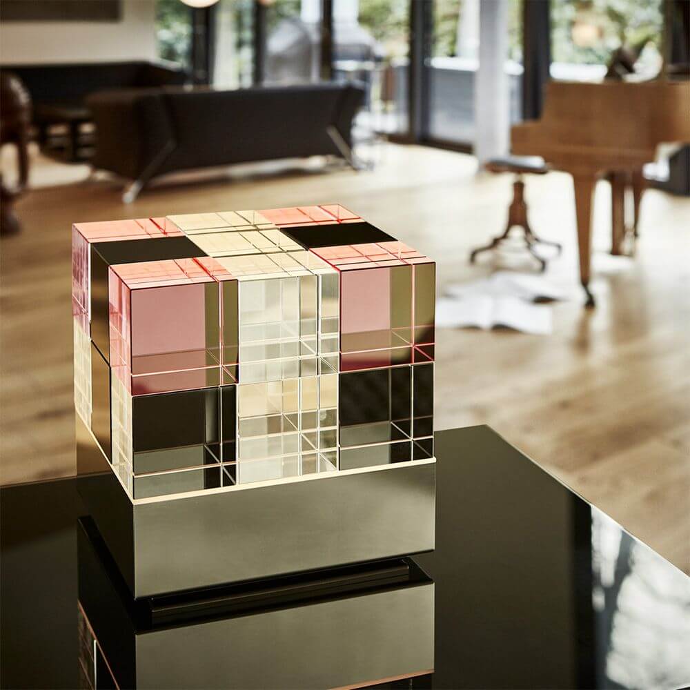 Tecnolumen Tischleuchte Cubelight Edelstahl Glas klar schwarz rosa auf modernem Tisch in stilvollem Innenraum.