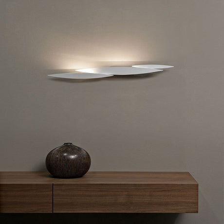 Terzani I Lucci Argentati LED Design-Wandlampe an Wand über einem Holztisch mit dekorativem Keramikgefäß.