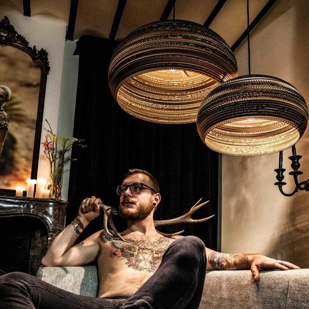 Dandy Pendellampe aus Karton oval im modernen Wohnraum mit einem Mann und stilvollem Interieur.