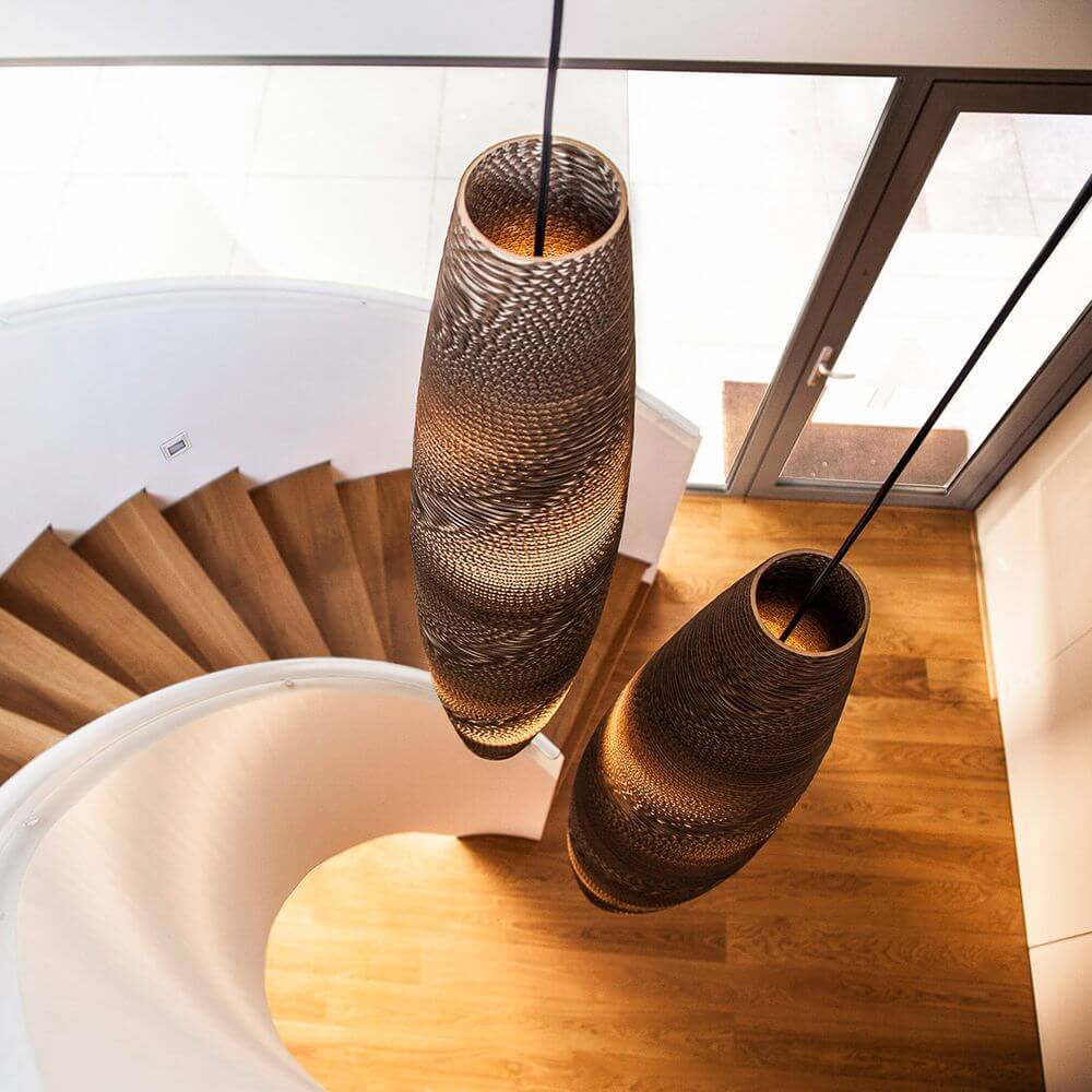 Zwei ovalen Pendelleuchten aus Pappe hängen über einer Holztreppe in modernem Innenraum.