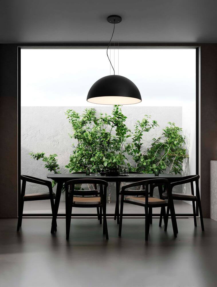 Tholos Pendelleuchte E27 in Schwarz über einem eleganten Esszimmertisch mit grünem Pflanzenhintergrund.