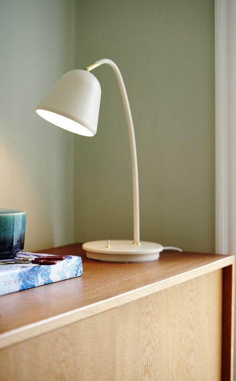 Bordlampe Fleur 15 på træhylde, nostalgisk design med messingdetaljer og justerbart lampehoved.
