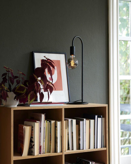 Tischlampe Paco mit minimalistischem Industriedesign und dekorativem Leuchtmittel auf einem Regal