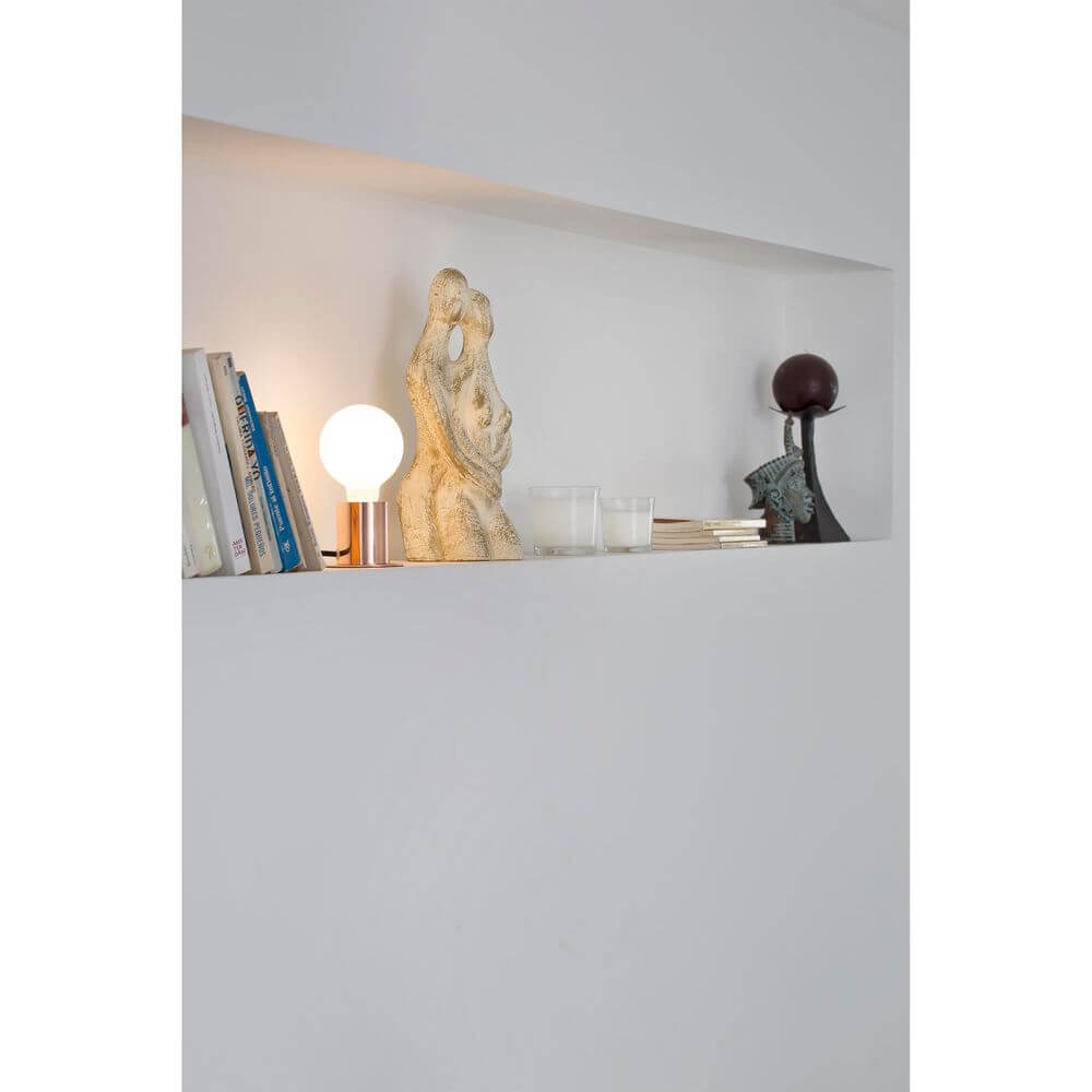 Tischlampe TEN Kupfer auf einem Regal, umgeben von Büchern und dekorativen Objekten.