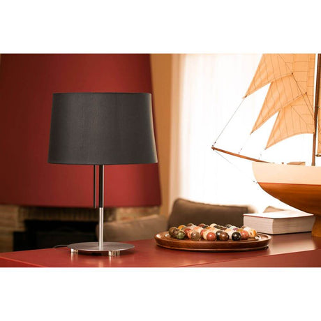 Tischlampe VOLTA Nickel-Matt, Schwarz auf Tisch mit Segelboot und bunten Kugeln.