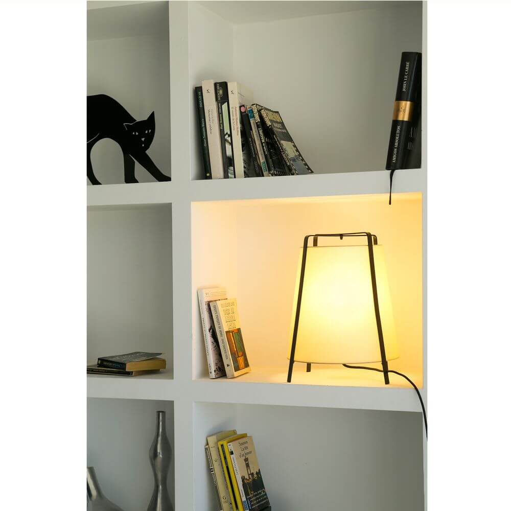 Tischleuchte AKANE Schwarz, Beige steht in einem Regal mit Büchern und einer schwarzen Katze.