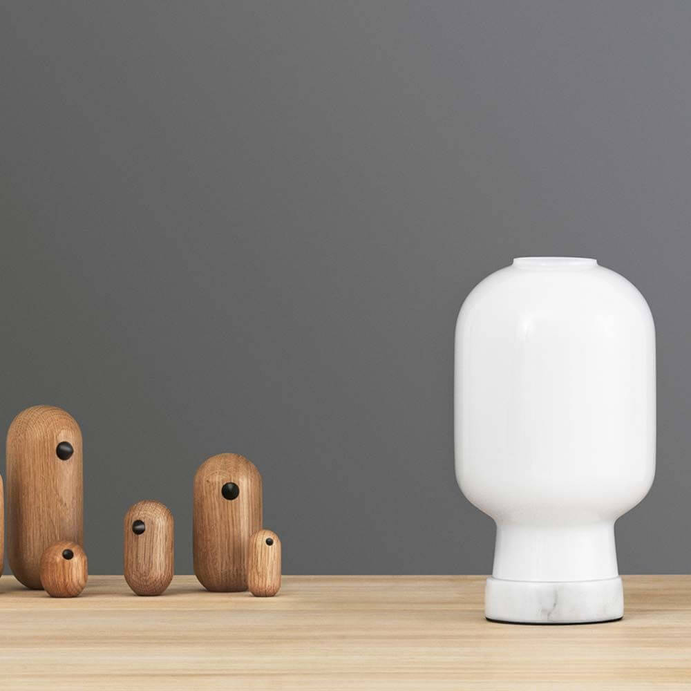 Tischleuchte Amp mit Marmorfuss Weiß neben Holzfiguren auf einem Tisch.