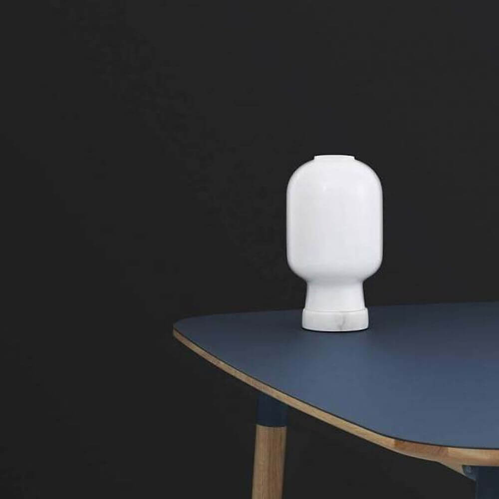 Tischleuchte Amp mit Marmorfuss Weiß auf einem Tisch mit blauem Tischblatt und schwarzem Hintergrund.
