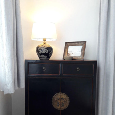 Lampada da tavolo Toulouse 42 cm in ceramica, nero-fango su una credenza nera con quadro incorniciato.