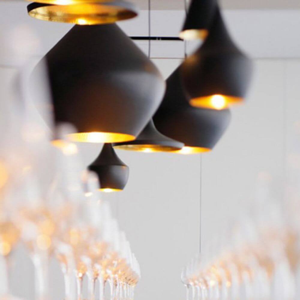 Tom Dixon Beat Wide LED Hängeleuchte in Schwarz, elegant aufgereiht über Gläsern.