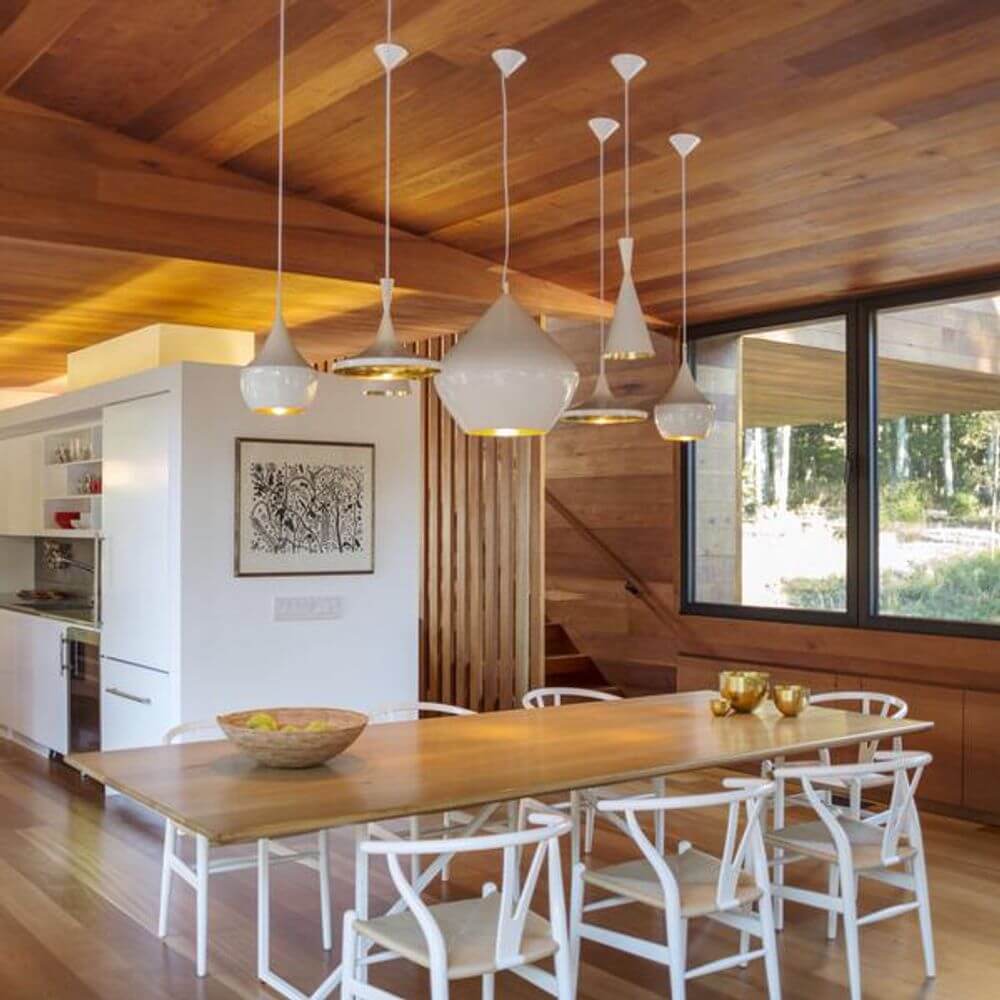 Moderne Esszimmer mit Holzdecke und stilvollen Hängeleuchten über einem großen Esstisch.