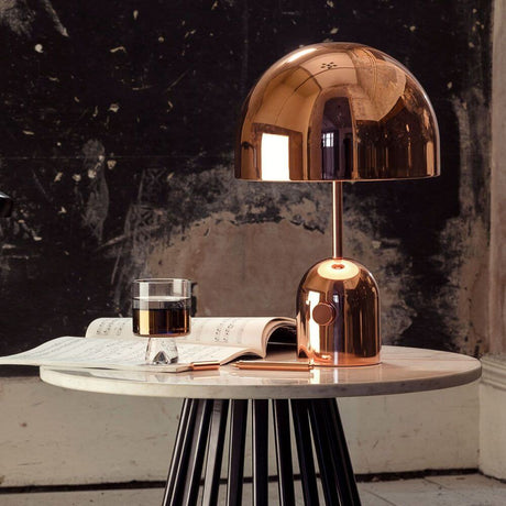 Tom Dixon Bell Tischleuchte mit Drehdimmer auf einem Tisch mit Buch und Getränk