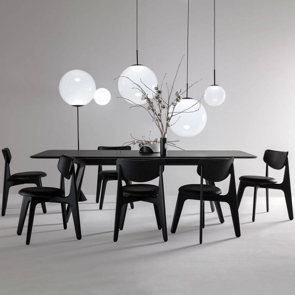 Tom Dixon Opal Kugelleuchte Pendel über einem modernen Esszimmertisch mit schwarzen Stühlen.