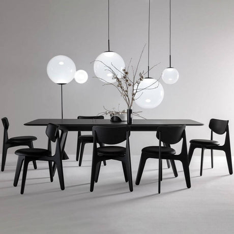 Tom Dixon Opal Kugelleuchte Pendel über einem modernen Esszimmertisch mit schwarzen Stühlen.