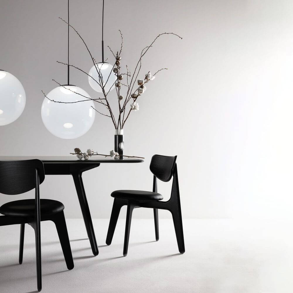 Tom Dixon Opal Kugelleuchte Pendel über einem Tisch mit schwarzen Stühlen und einem floralen Arrangement.