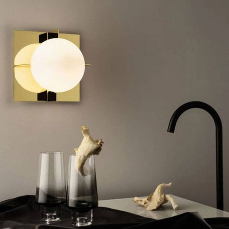 Tom Dixon Plane Wandleuchte Goldfarben in modernem Wohnzimmer mit Glaskugel und goldfarbenem Rahmen.