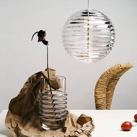 Tom Dixon Press Sphere Glas-Pendelleuchte über einer Vase mit einer verblühten Blume.