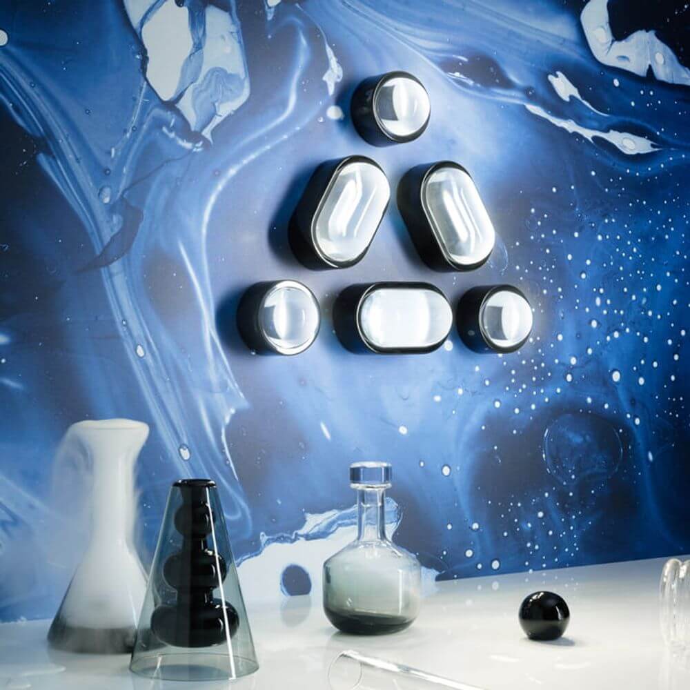 Tom Dixon Spot Wandleuchte mit Glaslinse an blauer Wand mit kreativem Design.