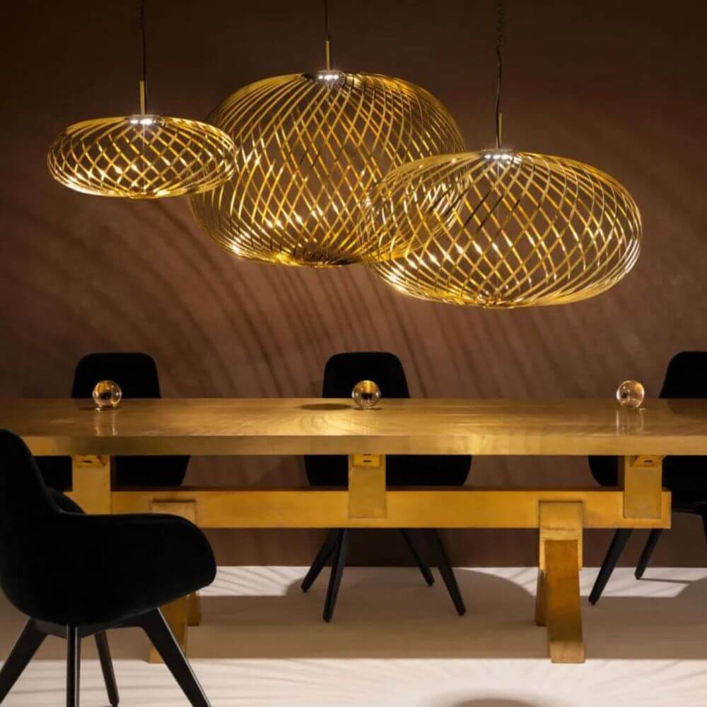 Tom Dixon Spring LED Hängelampe ausziehbar über einem goldenen Tisch mit schwarzen Stühlen.