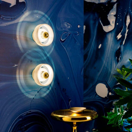 Tom Dixon Stone Wandlampe aus Marmor an einer blauen Wand mit Pflanzen und goldener Tischlampe.